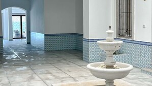 Un vaste couloir au sol carrelé mène à une pièce dont un mur est également carrelé et qui est dotée d’une porte blanche avec une barre métallique.