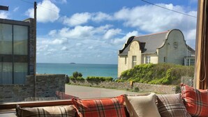A room with a view of the sea, a stone wall, and a building with a red roof. - Family Beach House for 2-9 people near Baby Bay in New Polzeath, North Cornwall (New Polzeath, Wadebridge)