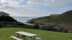A picnic table in a grassy area with a view of the sea and hills. - Family Beach House for 2-9 people near Baby Bay in New Polzeath, North Cornwall (New Polzeath, Wadebridge)