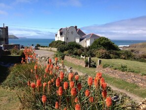 Ein Küstenhaus mit einem Steinweg, einem Garten mit leuchtend orangenen Blüten und Blick auf das Meer.