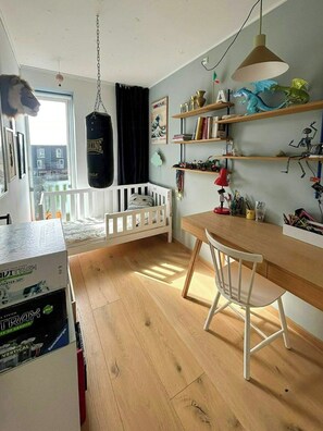 Una habitación con una cuna, un escritorio con una silla, un saco de boxeo colgante y estantes con diversos objetos.