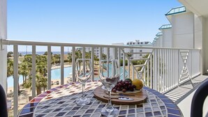 En balkon med et bord dækket til to, med udsigt til en swimmingpool og bygninger.