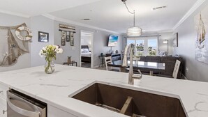 Et moderne køkken med en stor ø, et spiseområde med et glasbord og en stue med sofa og tv.