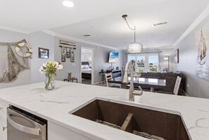 Eine moderne Küche mit einer großen Kochinsel, ein Essbereich mit einem Glastisch und ein Wohnzimmer mit einer Couch und Fernseher.