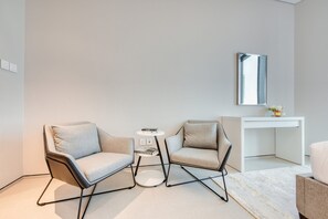 Ein modernes Zimmer mit zwei Sesseln, einem kleinen runden Tisch, einer weißen Kommode und einem Spiegel an der Wand.