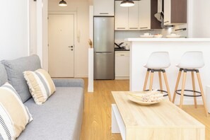 Ein modernes Wohnzimmer mit einer Couch, einem Holztisch und einer Küchenzeile mit Kühlschrank und Barhocker.