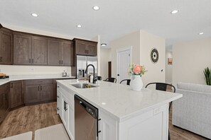 A modern kitchen with a central island, built-in appliances, and a dining area with a gray sofa. - Mountain View Home with Large Yard Near Salt Lake (Stansbury Park)