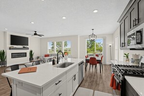 A modern kitchen with a central island, dining area, and a view of the outdoors. - Mountain View Home with Large Yard Near Salt Lake (Stansbury Park)