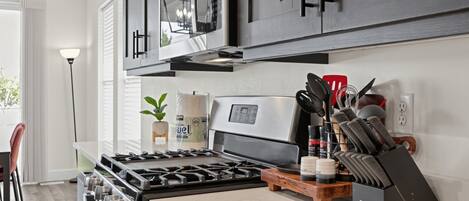 Una cocina moderna con estufa de acero inoxidable, microondas y tabla de cortar de madera.