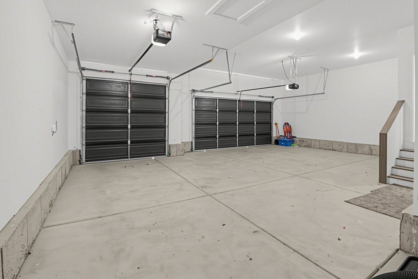 Un vaste espace intérieur doté de deux portes de garage fermées, d’un plancher en béton et d’un escalier menant à un niveau supérieur.