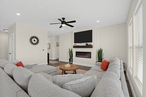 A modern living room with a grey sectional sofa, a round wooden coffee table, a fireplace, and a ceiling fan. - Mountain View Home with Large Yard Near Salt Lake (Stansbury Park)
