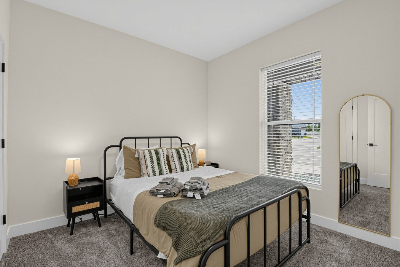 Une chambre à coucher avec un lit, des tables de chevet, une lampe, une fenêtre avec des stores et un miroir.