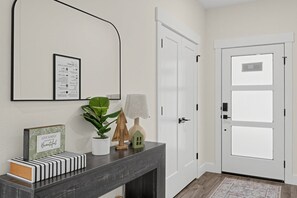 A hallway with a dark wood console table, a framed inspirational quote, a potted plant, a small wooden house model, and a door with a frosted glass panel. - Mountain View Home with Large Yard Near Salt Lake (Stansbury Park)