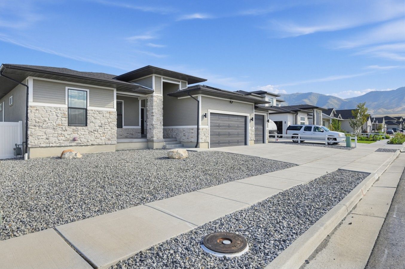 A residential area with modern houses, a driveway, and a mountain backdrop.