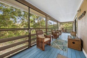 A covered porch with wooden chairs, a table, and a wicker chest.