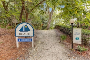 A pathway leading to a beach area with a sign indicating 'BEACH' and 'OWNER BIKE STORAGE'.