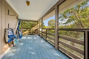A covered porch with a view of trees, a wooden railing, and a bench.