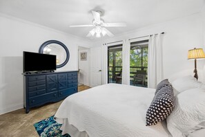 Une chambre Ă coucher comprenant un lit, une commode, un tĂ©lĂ©viseur, un ventilateur de plafond et une vue sur lâextĂ©rieur.