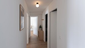 A hallway with wooden flooring, white walls, and a ceiling light fixture. - Cosy new apartment, terrace and small garden, magnificent mountain views (Le Monêtier-les-Bains)