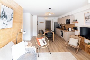 Ein modernes Wohnzimmer mit Sofa, Sessel, Essbereich und einer Küche mit Fernseher.