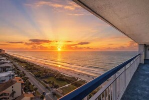 A sunset view from a balcony overlooking a beach with a road and buildings in the foreground. - “Castle in the Sky • Ocean Views
Penthouse (Myrtle Beach)