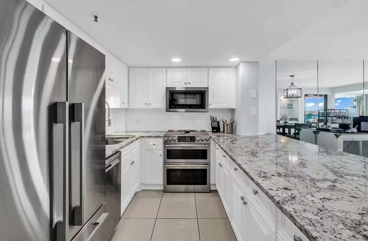 A modern kitchen with white cabinetry, stainless steel appliances, and a marble countertop.