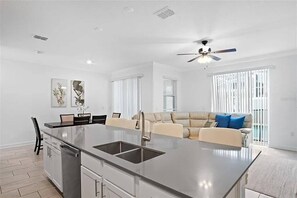 A modern kitchen with a central island, a dining area, and a living space with a sofa and a ceiling fan. - Go!#34 - CHAMPIONS GATE (Davenport)