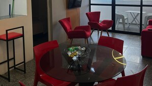 Una sala de reuniones moderna con una mesa de vidrio, sillas rojas y un amplio ventanal con vistas a edificios.