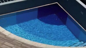 Una piscina con solárium de baldosas, barandilla metálica y tres sillas reclinables blancas.