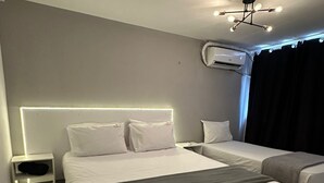 Habitación de hotel con una cama grande, una cama más pequeña, una mesita de noche, un equipo de aire acondicionado y una lámpara en el techo.