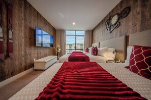 Ein Hotelzimmer mit einem großen Fenster, einem Fernseher, einem Bett mit roter Decke und einer Wanduhr.