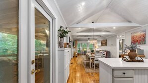 Cozinha ampla com piso de madeira, área de jantar com lustre e vista para o verde lá fora.
