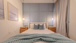 Ein Schlafzimmer mit einem Bett, zwei Nachttischen, einem Fenster mit Vorhängen und einer Wandleuchte.
