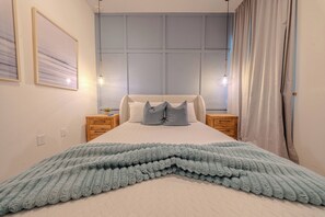 Ein Schlafzimmer mit einem Bett, zwei Nachttischen, einem Fenster mit Vorhängen und einer Wandleuchte.
