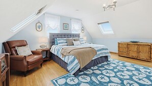 Un dormitorio con techo inclinado, una cama con colcha a rayas, un sillón de cuero, un armario de madera y una alfombra estampada.
