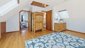 Una habitación amplia con suelo de madera, un ventanal grande, un ventilador de techo y un mueble de madera decorativo.