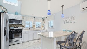 Una cocina moderna con armarios blancos, horno empotrado, una isla grande con taburetes de bar y una lámpara decorativa en el techo.