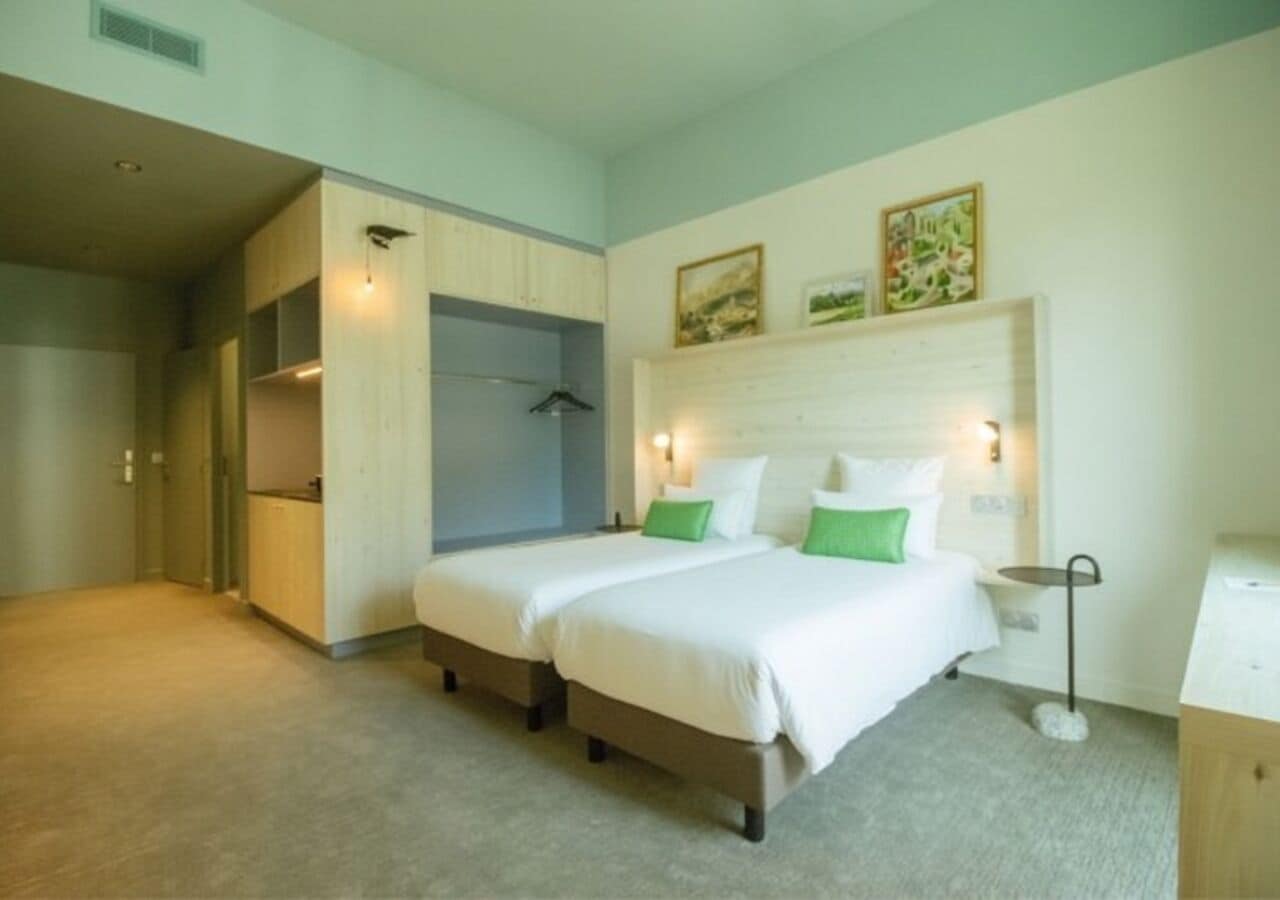A hotel room with two beds, a wardrobe, a bedside table, and a small desk.