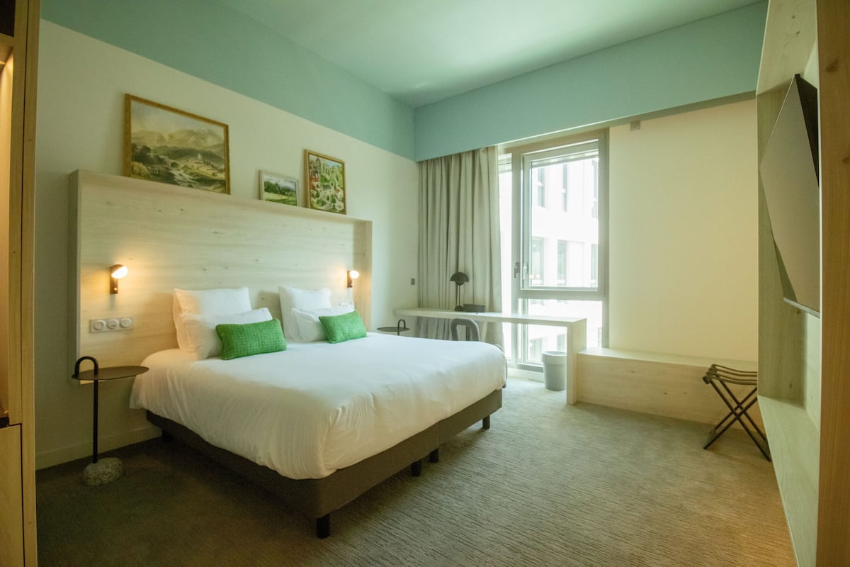A hotel room with a large bed, bedside lamps, a desk, and a window with curtains.