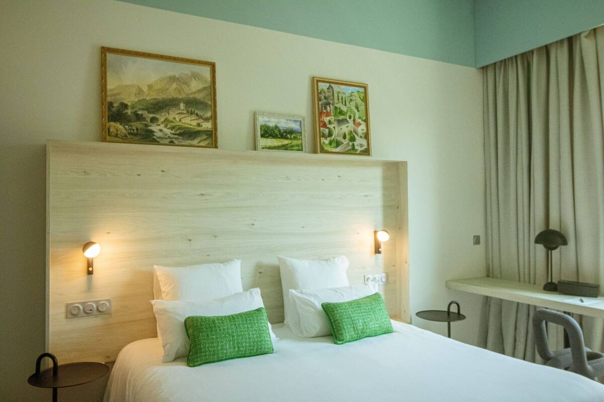 A hotel room with a large bed, two wall-mounted lamps, a desk, and a chair.