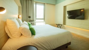 Hotellihuone, jossa on sänky, seinälle asennettu televisio, ikkuna verhoilla ja yöpöytä.
