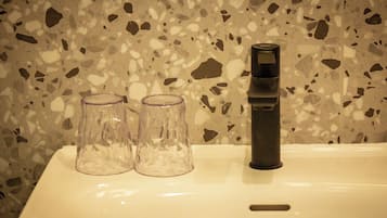 A bathroom sink with a terrazzo backsplash, two clear glass tumblers, and a black faucet.