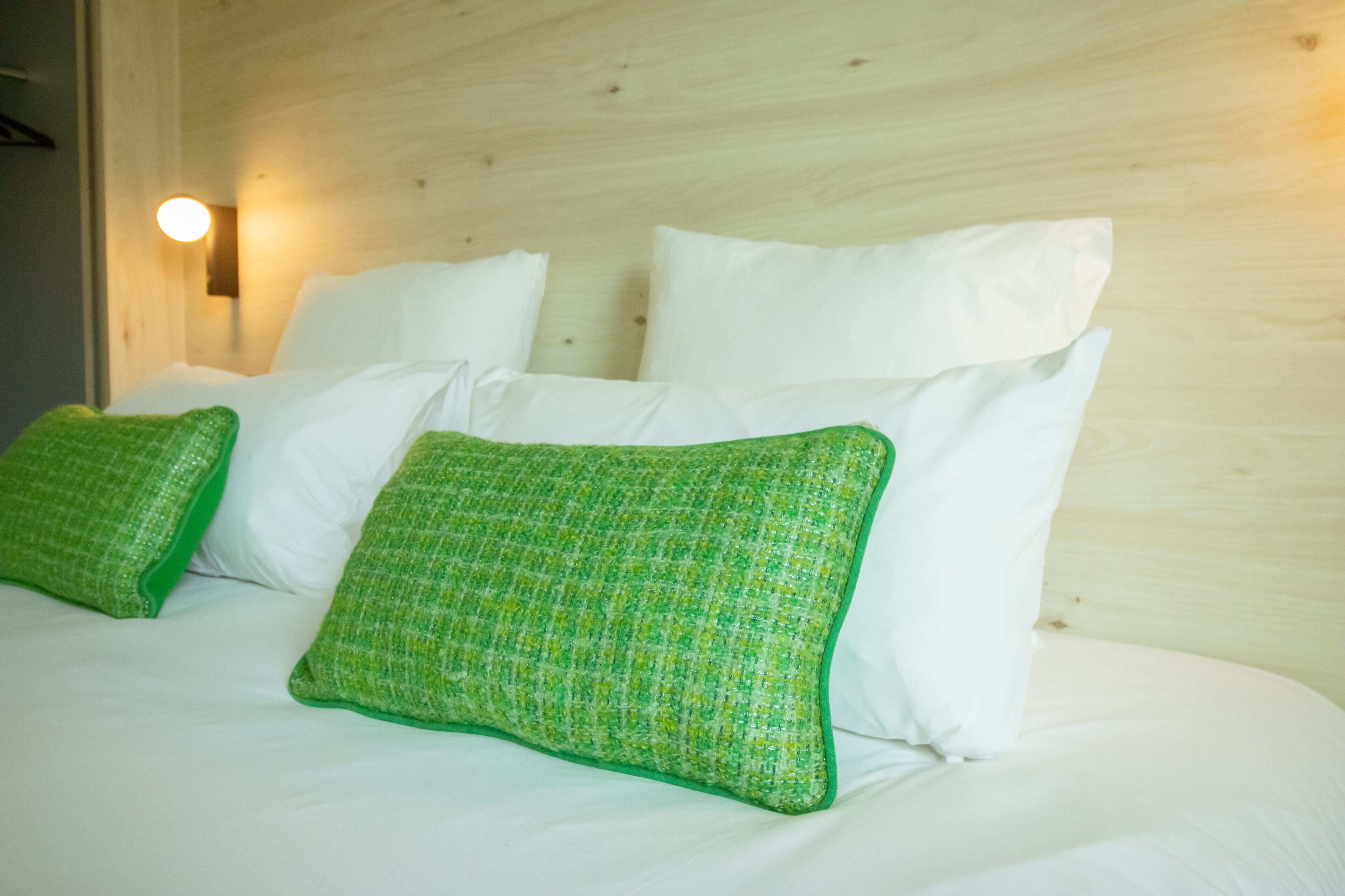 Ein Bett mit weißen und grünen Kissen, einem Holz-Kopfbrett und einer Wandleuchte.