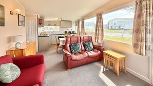 A compact living space with a kitchenette, a red sofa, a wooden table, and a window with curtains.