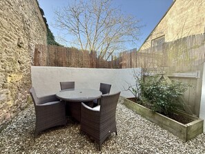 A patio with wicker furniture, a round table, and a wooden planter with plants. - One bed Character Cottage with Parking and Garden (East Portlemouth)