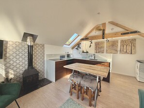 Une cuisine moderne dotée d’une cuisinière intégrée, un coin repas avec une table en bois et un espace nuit en mezzanine avec un puits de lumière.