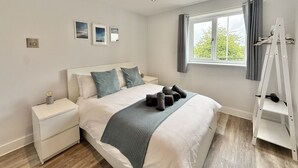 Ein Schlafzimmer mit einem Bett, Nachttischen, einem Fenster mit Vorhängen und einer weißen Leiter.