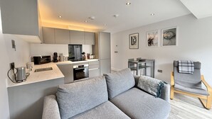 Ein modernes Wohnzimmer mit grauem Sofa, einem Holzstuhl, einer Küchenzeile und einem Esstisch.