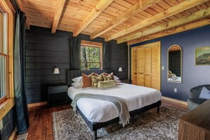 Ein Schlafzimmer mit Bett, Nachttischen, einem Fenster, einem Spiegel und einer Holzbalkendecke.