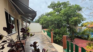 A covered outdoor area with potted plants, a tiled floor, and a green fence.